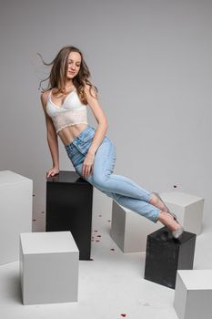 Pretty slim long haired caucasian girl in white top lingerie, blue jeans posing for studio portrait on gray background. High quality photo