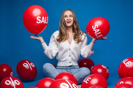 Happy beautiful lady holding on her palms two red balloons with the inscription sale, isolated on blue background. Shopping holiday concept