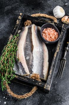 Fillet of Pickled marinated sea herring fish in a wooden tray. Black background. Top view.