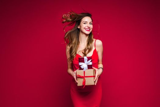 cheerful caucasian woman with attractive appearance with a lot of holiday gifts, picture isolated on red background