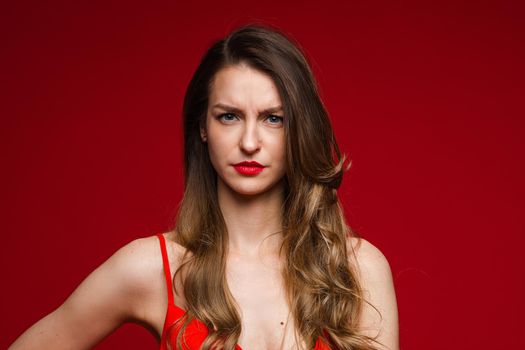 Head shot of young displeased serious female frowning on red studio background with copy space for advertising. High quality photo