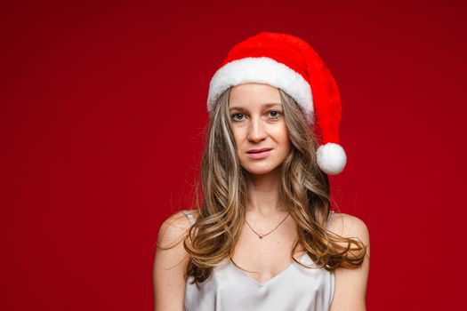 caucasian woman with attractive appearance with red and white christmas hat smiles, picture isolated on red background