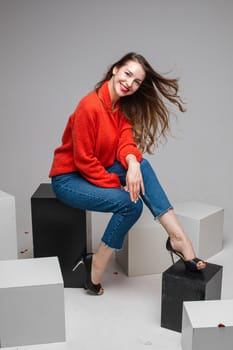 beautiufl caucasian woman with charming appearance sits on a white cube and looks to te camera, picture isolated on white background