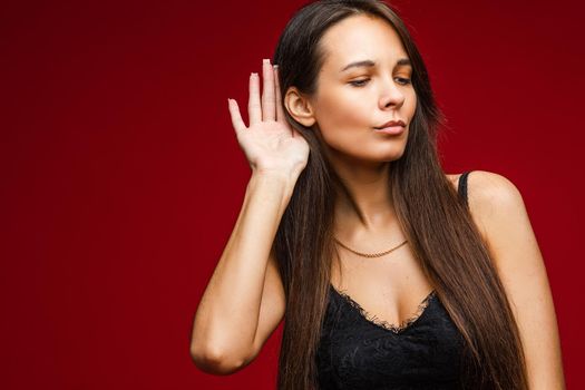 ccaucasian woman with attractive appearance listens someone, picture isolated on red background