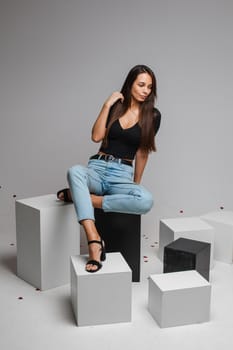 beautiufl caucasian woman with charming appearance sits on a white cube and looks to te camera, picture isolated on white background