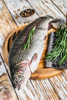 Rainbow trout on an wood board, with rosemary and cleaver. White wooden background. Top view.