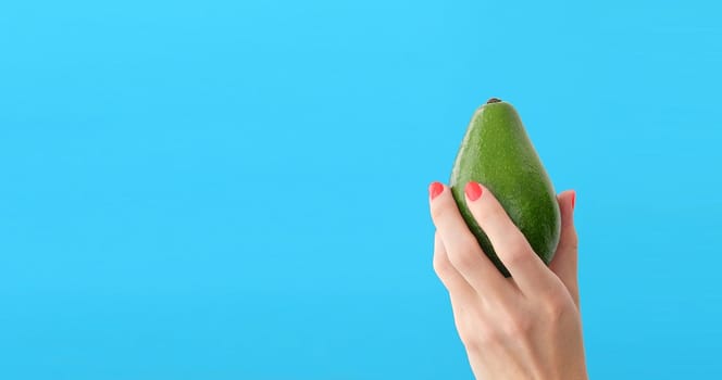 avocado in a hand of woman blue background. healthy food concept