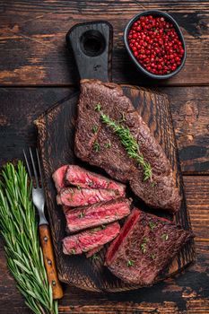Grilled sliced skirt beef meat steak on a cutting board with herbs. Dark wooden background. Top view.