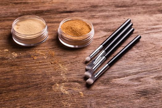 Loose compact mineral powder for face and a brushes for powder and visage on wooden background. Eco friendly and organic cosmetics