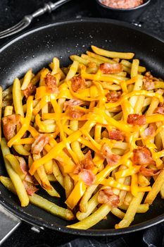 French fries baked with cheddar cheese and bacon in a pan. Black background. Top view.