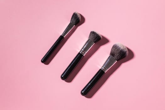 Various make-up brushes on pink background, top view. Cosmetics and beauty