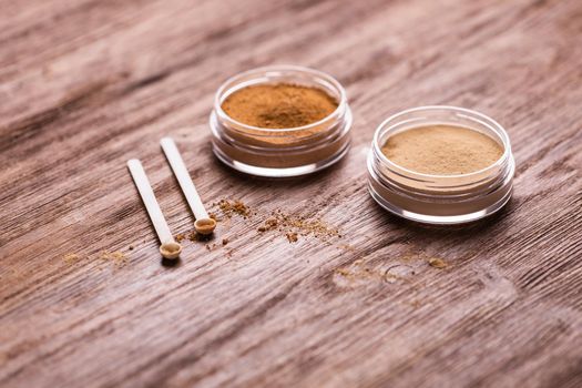 Mineral powder of different colors with spoon dispenser for make-up on wooden background.