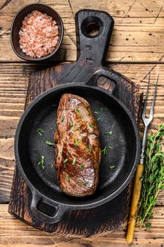 Grilled veal fillet meat steak in a pan with herbs. wooden background. Top view.