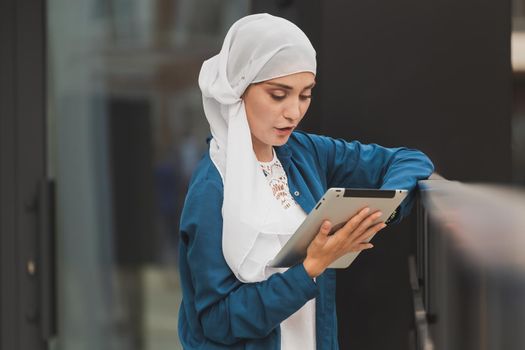 Smiling muslim girl using digital tablet, browsing Internet or social networks outdoor.