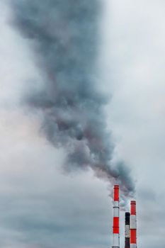 Problems of environmental pollution and ecology. Dark gray acrid smoke comes from a chimney of an industrial plant or thermal power plant against the background of the sky.