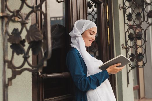Portrait of young muslim woman wearing hijab reading book outdoor