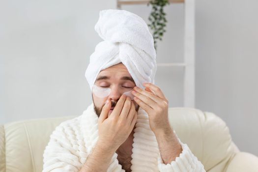 Young man with patches under the eyes at home. Concept of cosmetology for men.Spa at home, body and skin care.