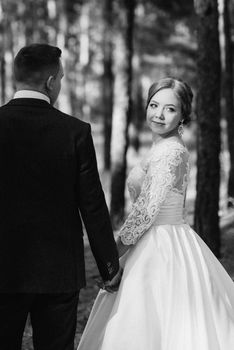 the bride and groom are walking in a pine forest on a bright day