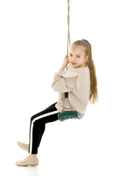Beautiful little girl swinging in the studio on a swing. Concept of a happy childhood, family well-being.