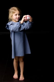 Beautiful Smiling Girl Taking Photo with Toy Camera, Adorable Barefoot Kid in Blue Dress Posing in Studio, Full Length Portrait of Cute Stylish Blonde Girl Isolated on Black Background