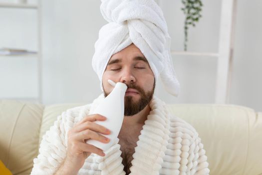 Bearded male with towel on his head applying body lotion cream. Guy smile when smell lotion cream on hand. Spa, body and skin care for man concept.