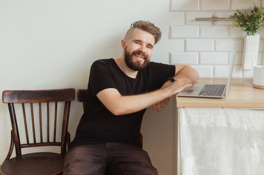 Happy smiling young man watching and working on computer laptop at home. Technologies, remote work and social networks.