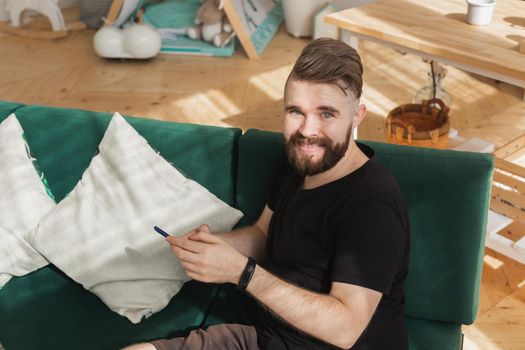 Relaxed man using a smartphone sitting on a green couch in the living room at home