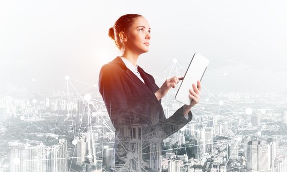 Young businesswoman using tablet computer. Double exposure concept with modern cityscape and beautiful woman in business suit. Digital technology in property management and development company.