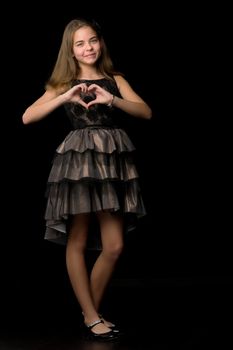 Cute little girl makes a heart with her hands and smiles on a black background.