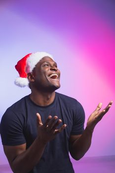 Portrait of positive handsome man in santa hat and casual t-shirt on colourful background, christmas time. Winter holidays and emotional people concept