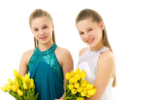 Beautiful girls sitting on the floor with a bouquet of yellow tulips, smiling sisters in summer dresses, portrait of pretty teenage girls on a white background