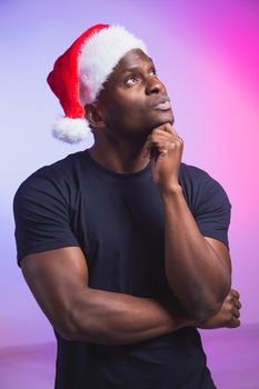 Portrait of positive handsome man in santa hat and casual t-shirt on colourful background, christmas time. Winter holidays and emotional people concept