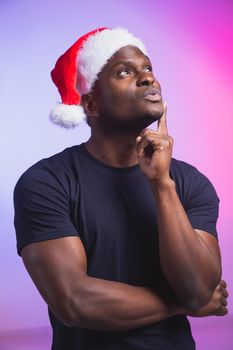 Portrait of positive handsome man in santa hat and casual t-shirt on colourful background, christmas time. Winter holidays and emotional people concept