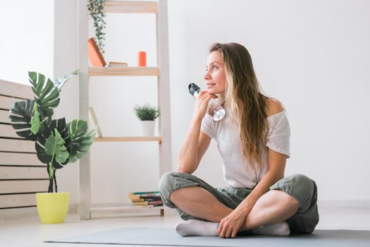 Positive girl sitting on fitness mat resting after pilates or yoga practice. Mindfulness and wellbeing concept