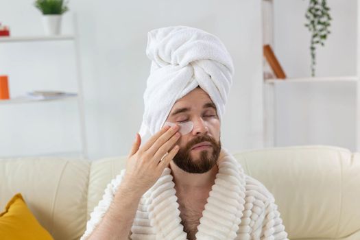 Bearded man applying eye patches on his face. Wrinkles and face home care for men