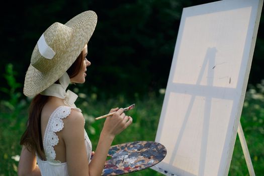 Woman in white dress paints a picture on nature easel. High quality photo