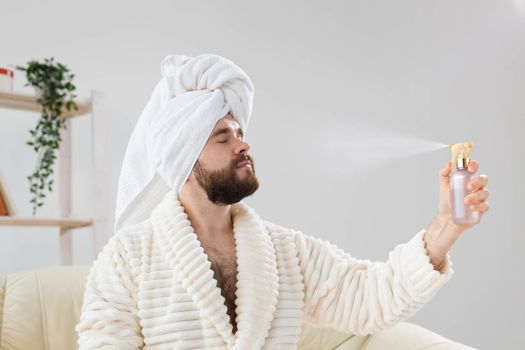 Bearded male with bath towel on his head applying spray water treatment on face. Spa, body and skin care for man concept