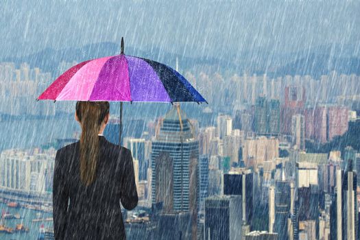 business woman holding multicolored umbrella with falling rain at city background