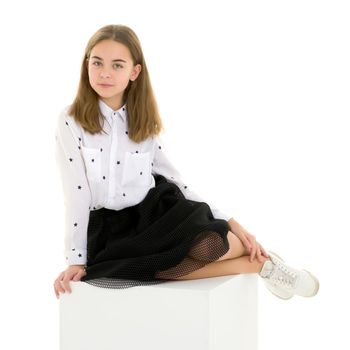 Front View Portrait of Beautiful Blonde Girl in Elegant Dress Sitting on Cube in Studio, Cheerful Long Haired Girl Wearing Fashionable Stylish Clothes Posing Against White Background