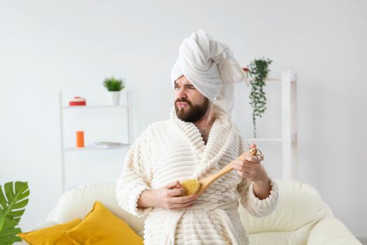 Funny handsome man pretends to play on massage brush as a guitar. Fun, spa and humor concept