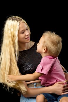 The older sister and younger brother are hugging in the studio on a black background. Childhood concept.