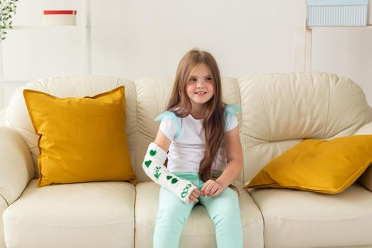 Child with a cast on a broken wrist or arm smiling and having fun on a couch. Positive attitude, recovery and kid.