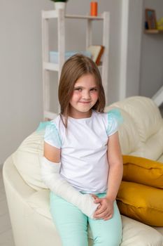 Child with a cast on a broken wrist or arm smiling and having fun on a couch. Positive attitude, recovery and kid.