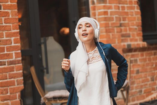 Middle eastern woman in hijab listening music with headphones and dancing outdoors. Woman independence and feminism concept