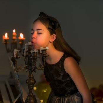 Beautiful Blonde Long Haired Girl Blowing out Candles in Vintage Chandelier, Side View of Charming Preteen Stylish Girl Sitting on Blurred Background Lighting by Warm Candle Light