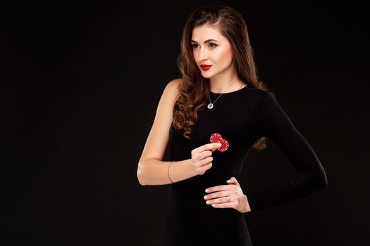 Sexy curly hair brunette in black dress posing with chips in her hands, poker concept black background. Casino, poker, Roulette Blackjack Spin.