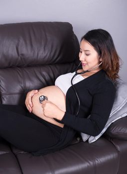 pregnant woman listening baby's heartbeat with stethoscope placed on her belly