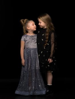 Two cute little girls posing in the studio on a black background. Style and fashion concept, layout for magazine cover.