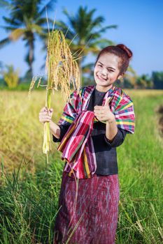 woman showing thumb up and holding rice in field, Thailand