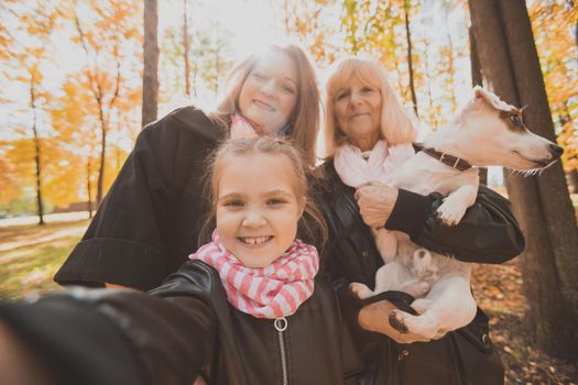 Three generations of women and dog feel fun look at camera posing for self-portrait picture together, funny excited child, mom and grandmother have fun enjoy weekend take selfie on gadget on autumn park